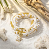 Lot de 5 bracelets bohèmes avec perles, coquillages et étoiles de mer posés sur le sable blanc avec des éléments marins