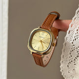 Montre carrée vintage femme avec bracelet en cuir marron et cadran doré, tenue par une main