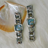 Deux montres femme luxe bohème argentées, cadrans nacre bleus, sur coquillage
