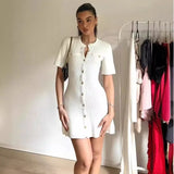 Femme en robe courte tricotée blanche avec boutons métal, style épuré pour l'automne.