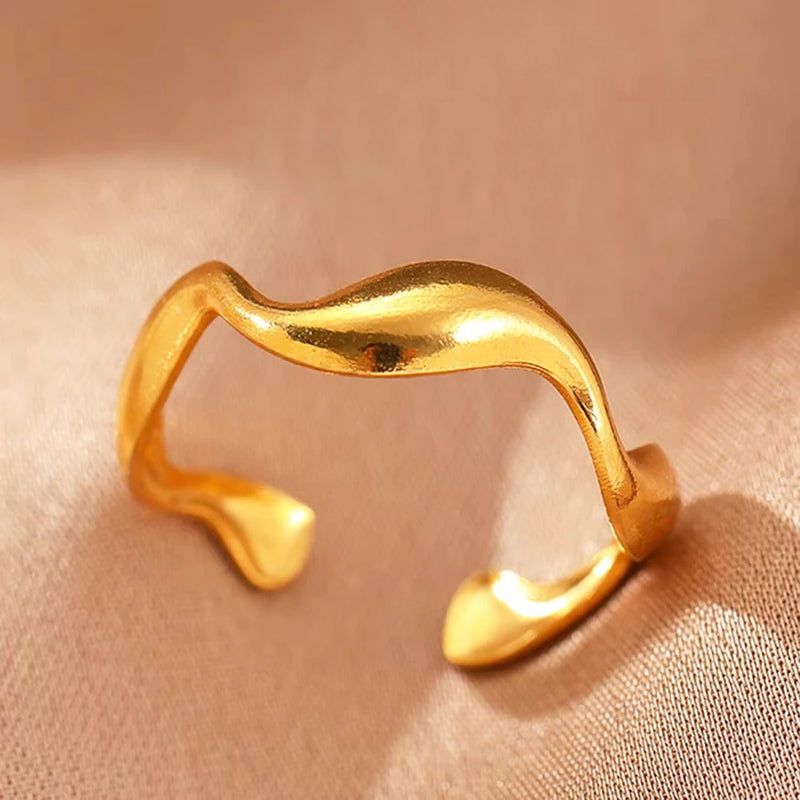 Bague dorée géométrique ondulée sur tissu satiné beige