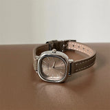 Montre carrée vintage pour femme avec bracelet en cuir beige et cadran argenté, posée sur une surface marron