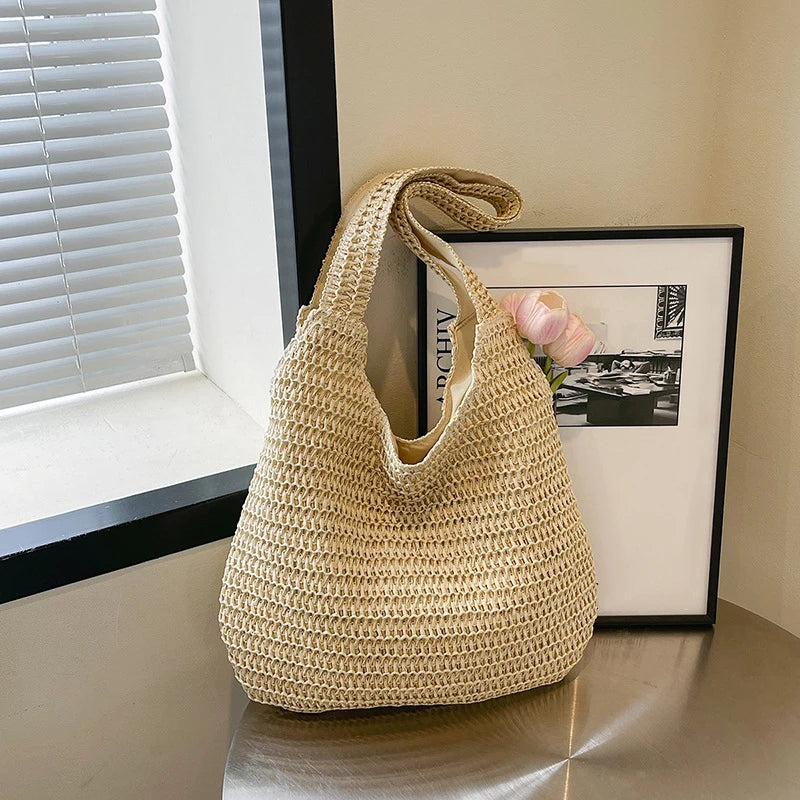 Grand sac cabas en paille tressée beige clair posé sur une table avec une fleur rose pâle