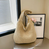 Grand sac cabas en paille tressée beige clair posé sur une table avec une fleur rose pâle