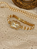 Montre femme dorée avec cadran rectangulaire et bracelet double rang de perles sur dentelle