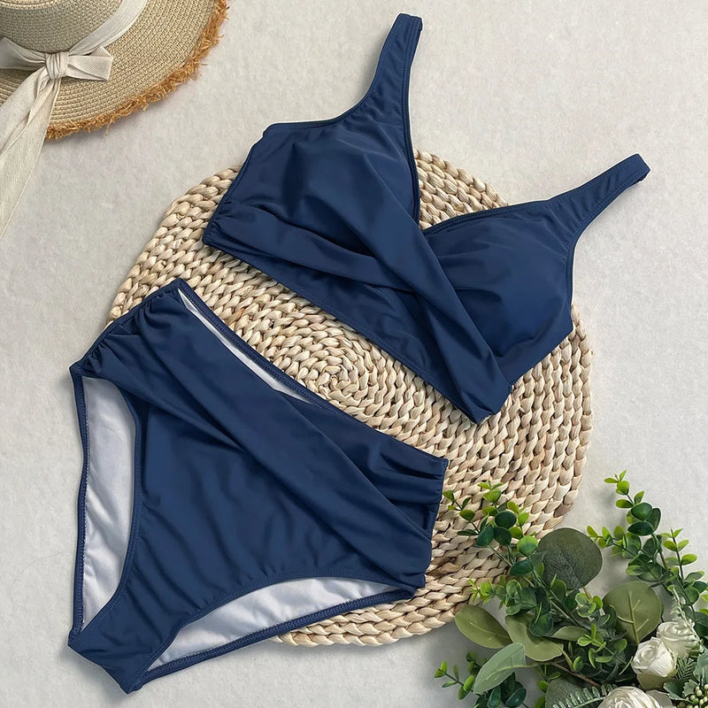 Ensemble bikini taille haute bleu marine avec haut croisé et culotte drapée, posé sur une natte en osier