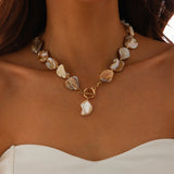 Collier bohème composé de perles nacrées irrégulières et d'un pendentif perle baroque sur un décolleté blanc