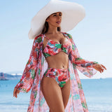 Femme en maillot de bain 3 pièces imprimé tropical rouge et vert, marchant avec grâce sur la plage