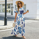 Femme portant une robe longue fleurie bleue et grise avec manches à volants, chapeau de paille et lunettes de soleil en ville