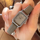 Montre femme vintage carrée GEDI, bracelet cuir gris, boîtier argenté, tenue par une main