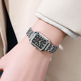 Montre femme carrée argentée avec cadran noir sur fond blanc