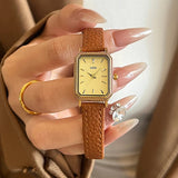 Montre femme vintage carrée GEDI, bracelet cuir gris, boîtier doré, tenue par une main