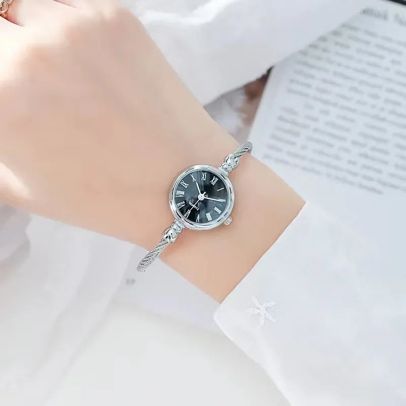 Montre bracelet argentée avec cadran noir à chiffres romains portée par une femme
