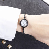 Montre bracelet noire avec cadran blanc à chiffres romains portée par une femme