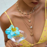 Collier multi-rangs doré avec détails marins porté avec un haut de maillot de bain jaune