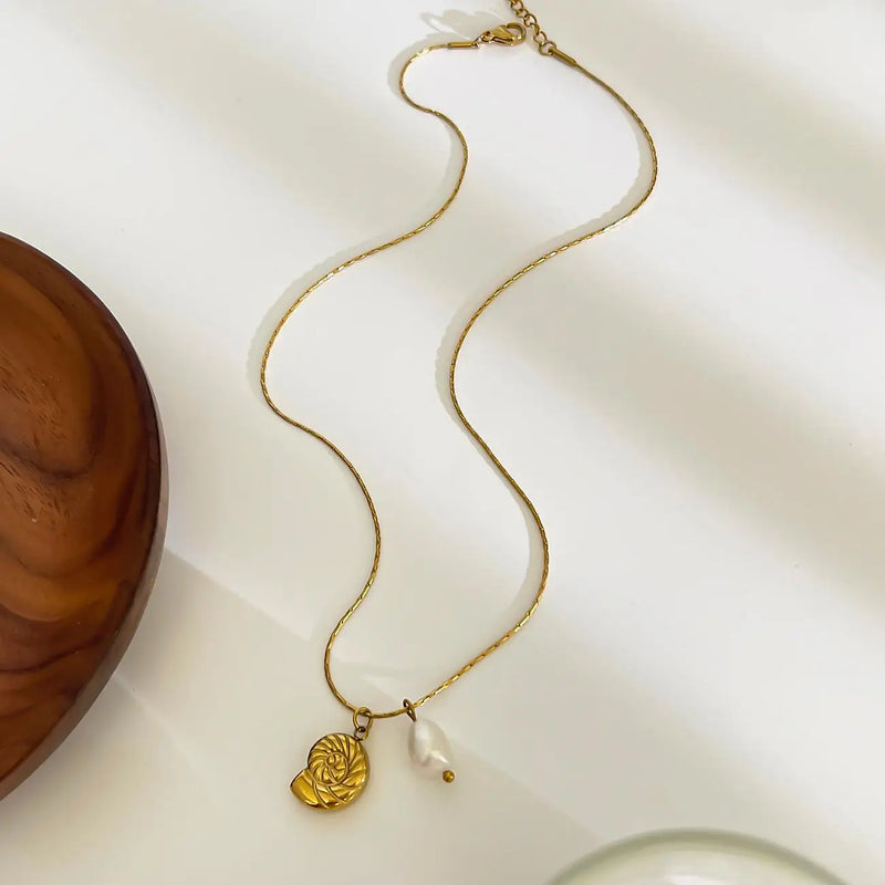 Collier doré avec pendentif coquillage et perle sur fond blanc