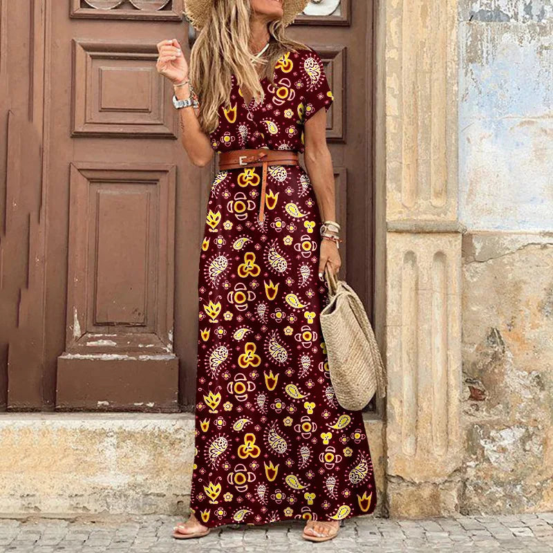 Femme portant une robe longue fleurie bohème bordeaux avec des motifs paisley jaunes, ceinture marron et chapeau de paille