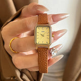 Montre femme vintage carrée GEDI, bracelet cuir marron, boîtier doré, tenue par une main