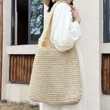 Femme en robe blanche portant le sac de plage tressé beige sur l'épaule