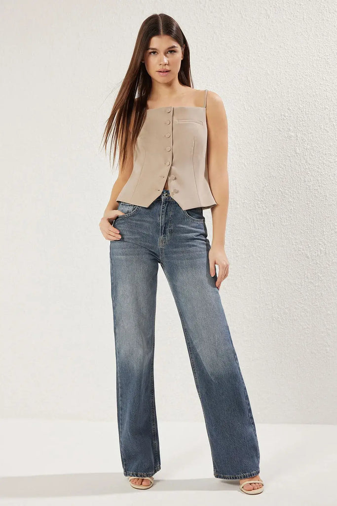 Modèle portant un jean vintage taille haute évasé 100% coton avec un haut beige à boutons.
