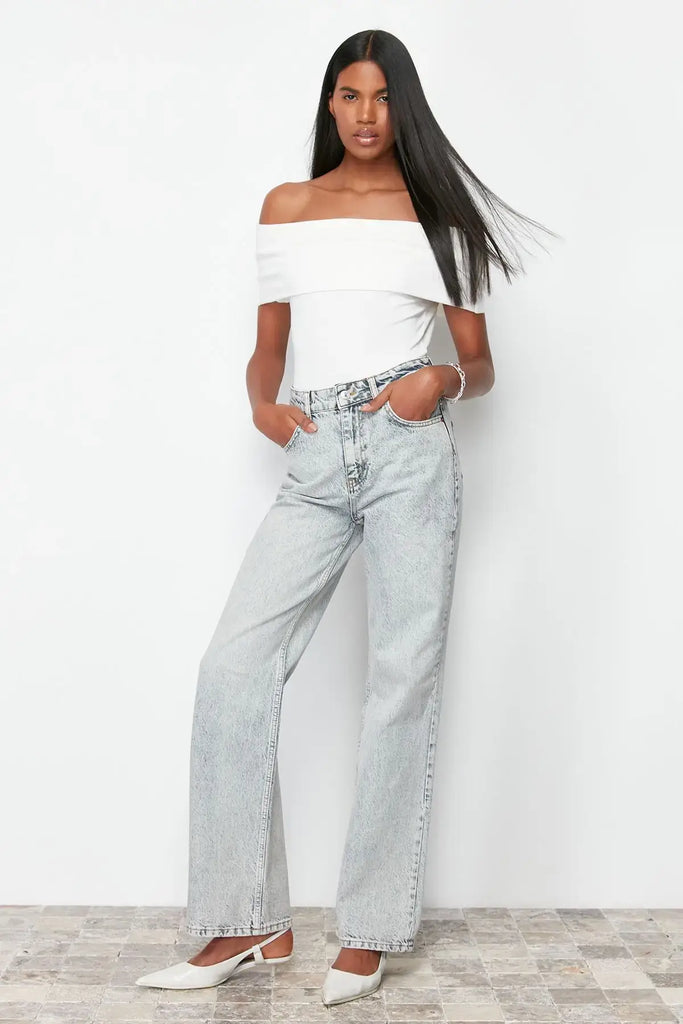 Femme portant un jean vintage taille haute évasé en coton et un top blanc décontracté, posant sur un fond neutre.
