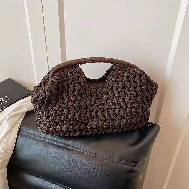 Sac à main en paille tressée marron foncé, posé sur un fauteuil en cuir