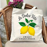Sac fourre-tout en toile blanc avec motif La Dolce Vita et citrons, posé sur une chaise en rotin