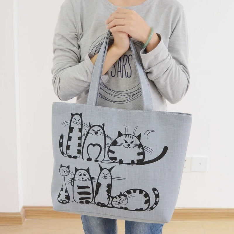 Femme portant un sac fourre-tout en toile gris clair avec des illustrations de chats noirs, style bohème et décontracté.