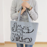 Femme portant un sac fourre-tout en toile gris clair avec des illustrations de chats noirs, style bohème et décontracté.