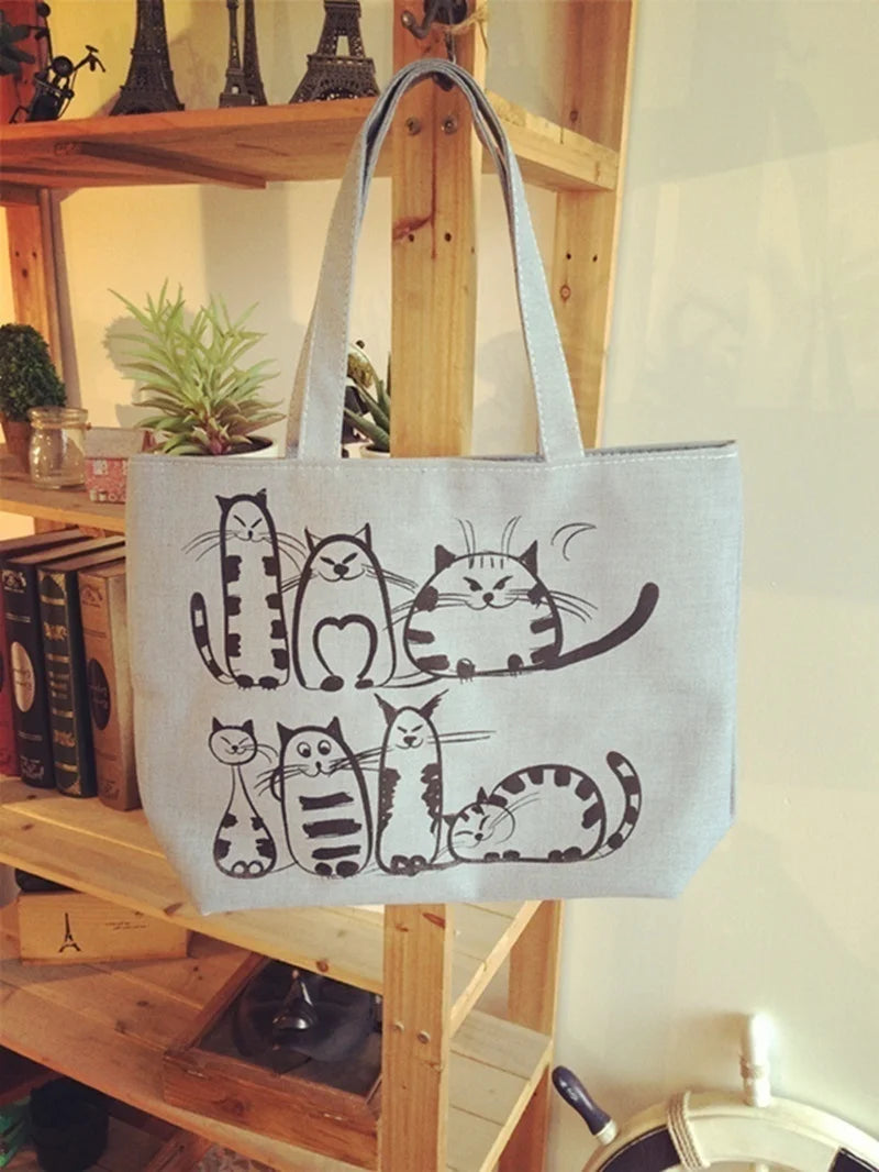 Sac fourre-tout en toile gris clair avec motif de chats posé sur une étagère en bois, ambiance cosy et naturelle.