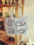 Sac fourre-tout en toile gris clair avec motif de chats posé sur une étagère en bois, ambiance cosy et naturelle.