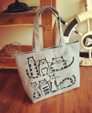 Sac à main en toile gris clair orné de dessins de chats, posé sur un meuble en bois avec décoration marine, esprit estival.