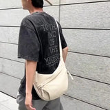 Homme portant un sac hobo bandoulière beige sur une épaule, look décontracté