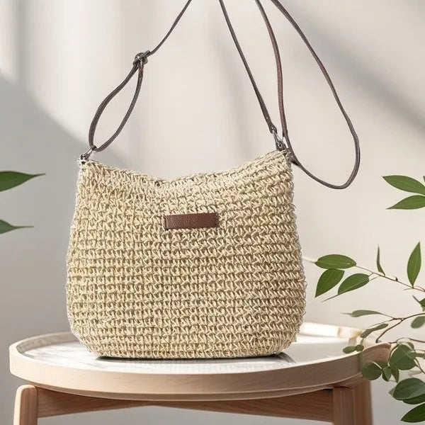 Sac bandoulière en paille tressée couleur beige avec anse marron posé sur une table basse