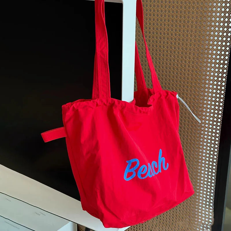 Sac de plage rouge 'Beach' accroché, motif lettre bleu