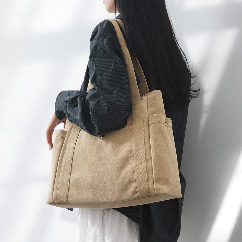 Femme portant un grand sac cabas en toile camel à l'épaule, vue de dos, pour illustrer sa taille et son porté