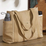 Sac cabas en toile camel posé sur une table en bois, avec un parapluie et une gourde rangés dans les poches latérales